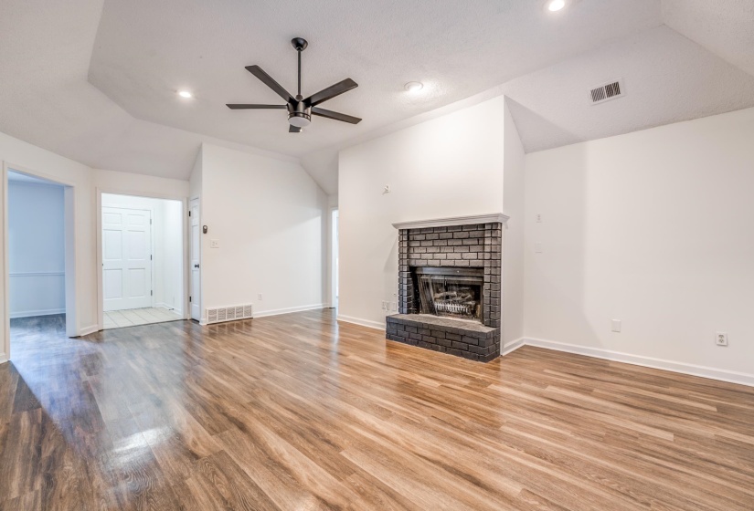 Unfurnished living room featuring vaulted ceiling, a brick fireplace, ceiling fan, wood finished floors, and recessed lighting