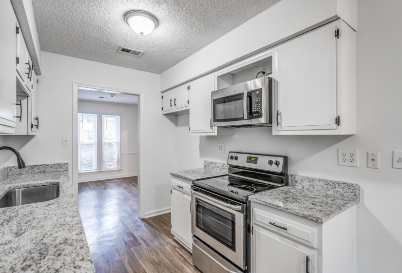 Kitchen featuring appliances with stainless steel finishes, dark wood finished floors, a textured ceiling, light stone countertops, and white cabinetry
