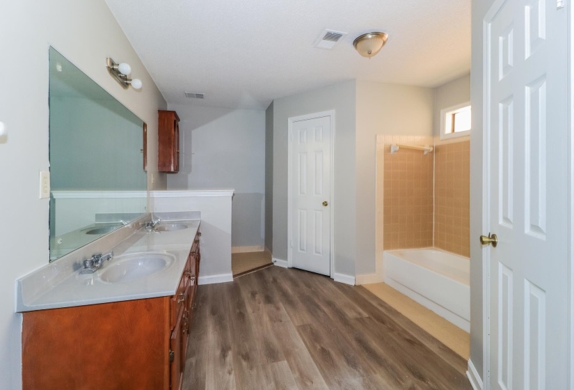 Bathroom featuring washtub / shower combination, double vanity, and dark wood finished floors