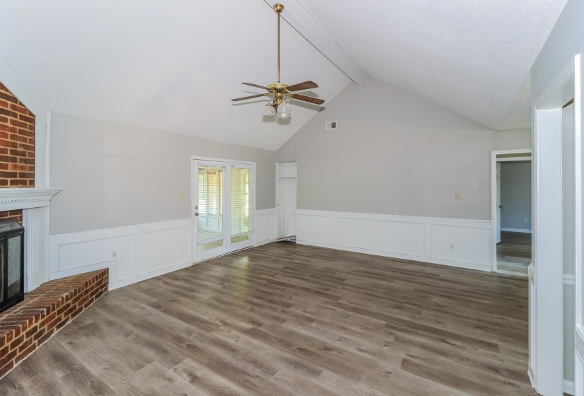Unfurnished living room featuring beamed ceiling, a fireplace, wainscoting, a decorative wall, and wood finished floors
