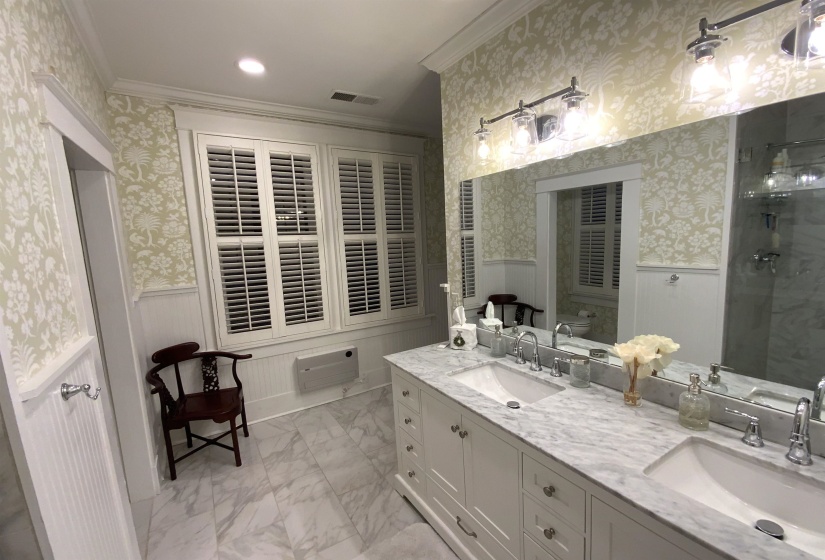 Bathroom featuring wainscoting, wallpapered walls, a stall shower, double vanity, and a decorative wall