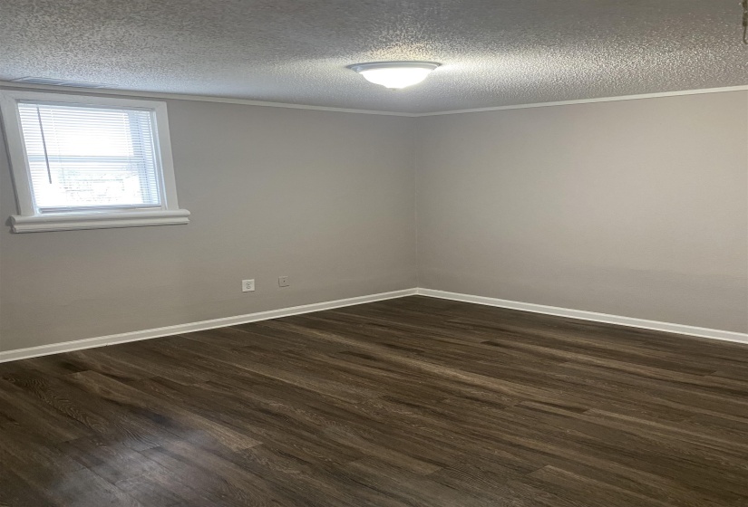 Empty room with dark wood finished floors, a textured ceiling, and ornamental molding