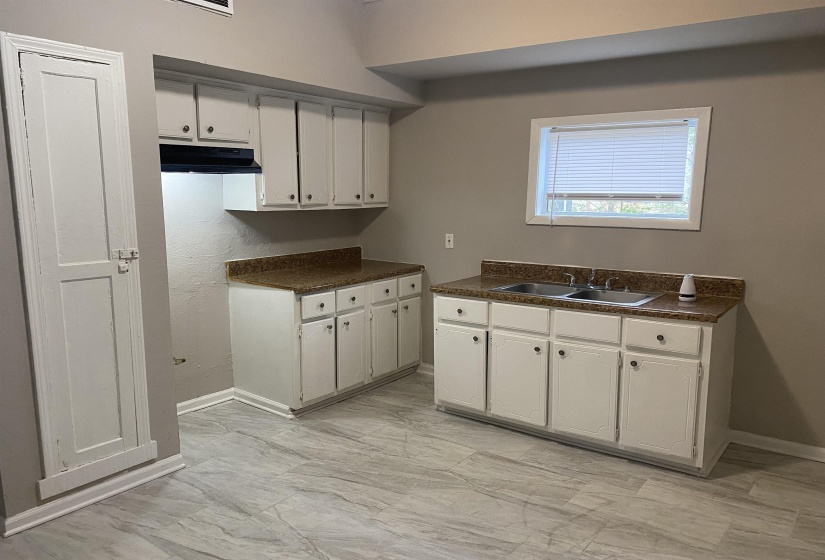 Kitchen featuring white cabinetry, dark countertops, under cabinet range hood, and light marble finish flooring