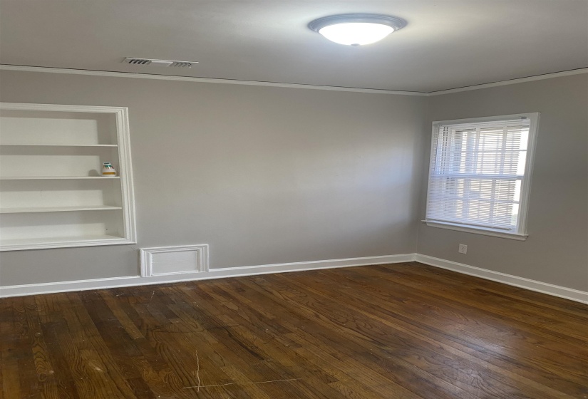 Empty room featuring built in features, dark wood-style flooring, and ornamental molding