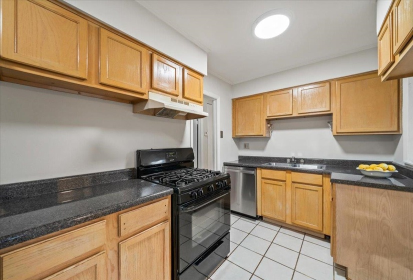 Kitchen with black gas range oven, under cabinet range hood, light tile patterned flooring, and dishwasher