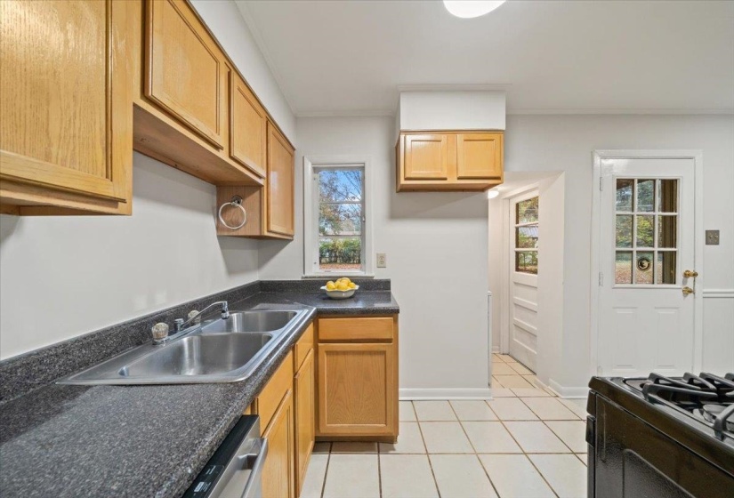 Kitchen with light tile patterned floors, dark countertops, black range with gas cooktop, crown molding, and stainless steel dishwasher
