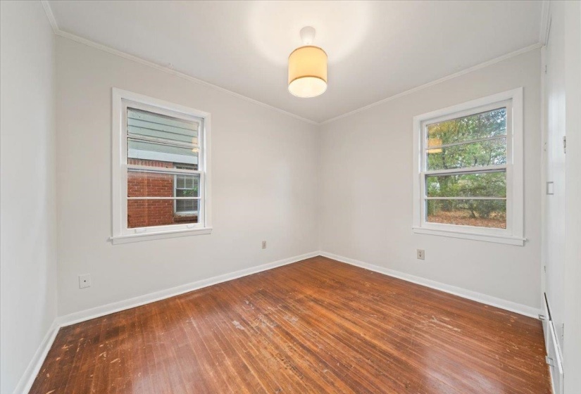 Empty room with dark wood finished floors, ornamental molding, and healthy amount of natural light