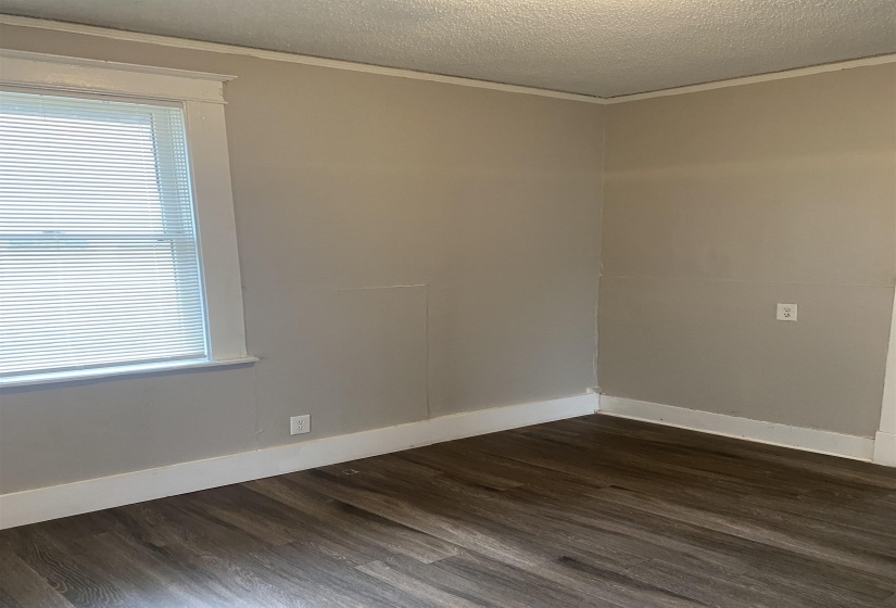 Empty room with dark wood finished floors, a textured ceiling, and crown molding