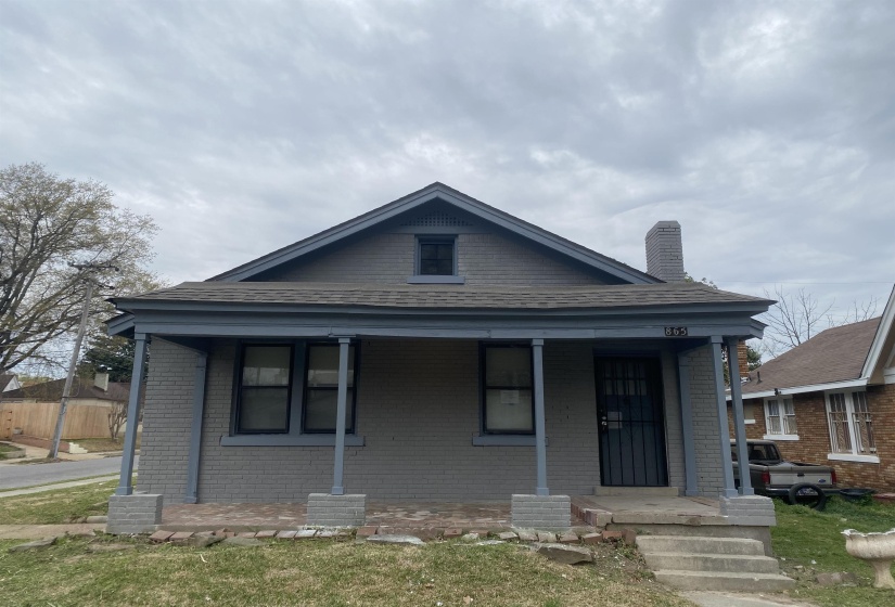 View of front of house featuring brick siding, covered porch, a chimney, and a front lawn