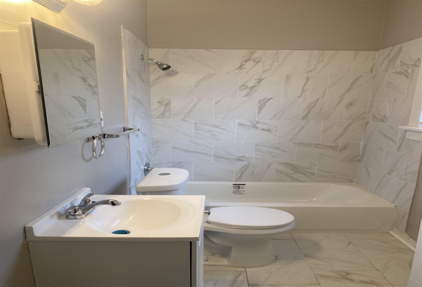 Bathroom with marble finish flooring, vanity, and washtub / shower combination