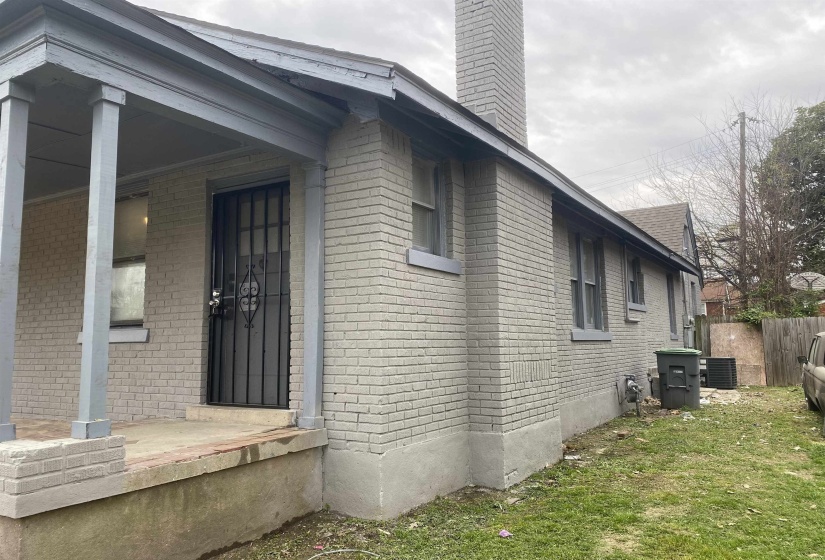 View of property exterior featuring a chimney, brick siding, and a porch
