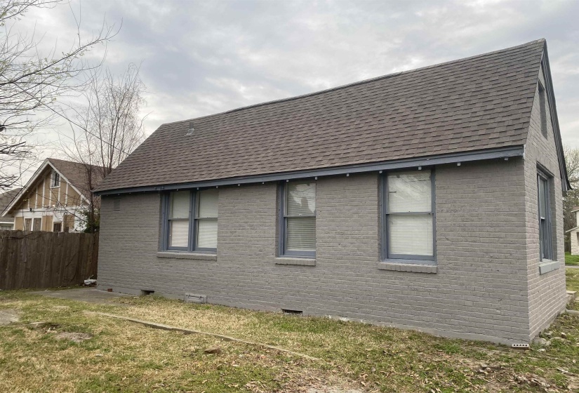 View of side of home with brick siding, crawl space, and roof with shingles