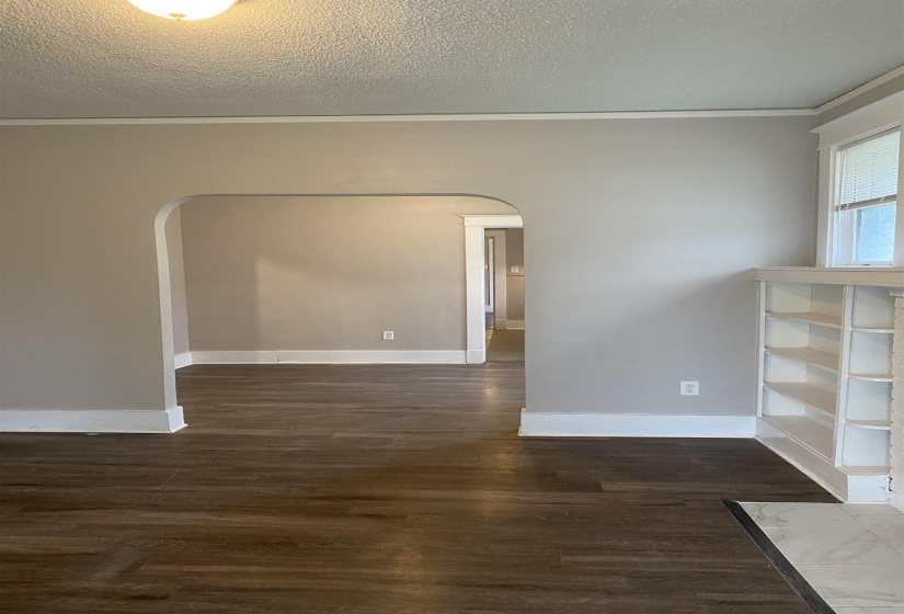 Empty room featuring dark wood-style flooring, arched walkways, a textured ceiling, and crown molding
