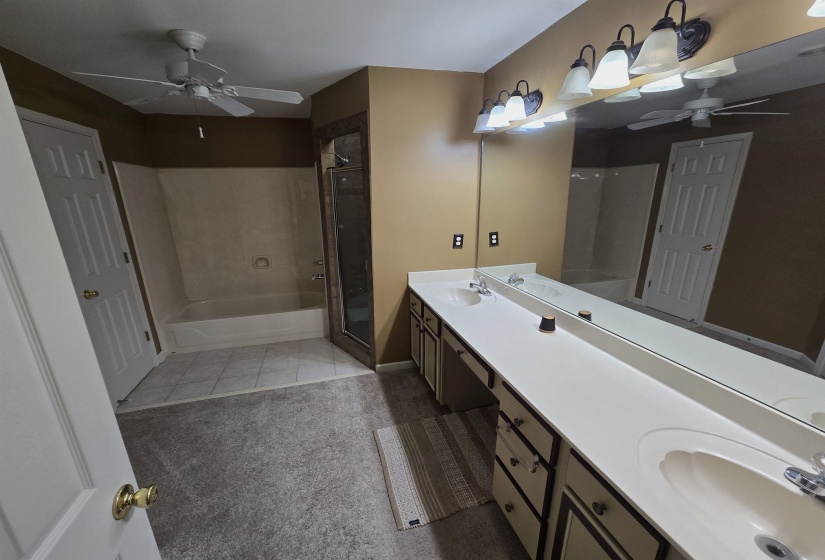 Bathroom featuring a ceiling fan, a bath, double vanity, a shower stall, and light carpet