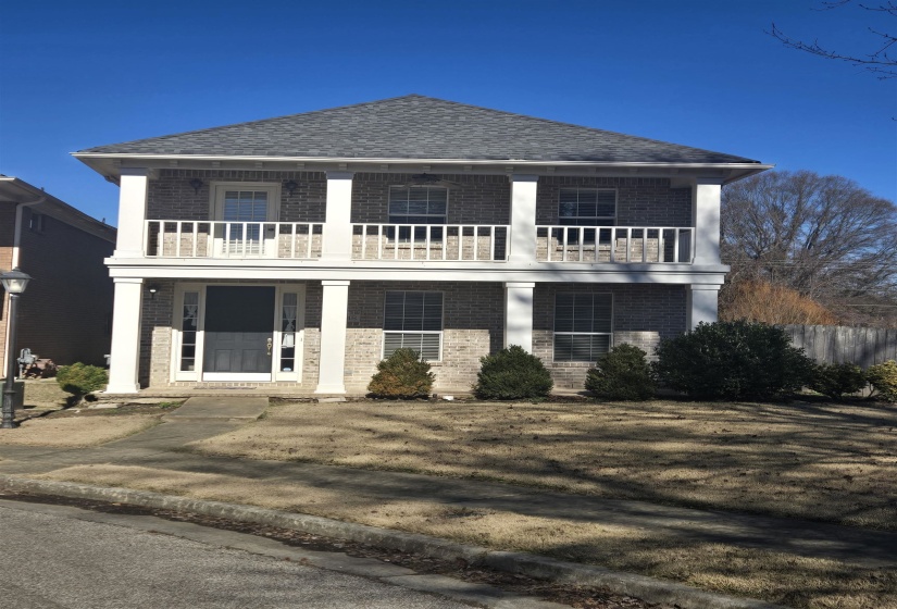 View of front of house featuring brick siding, a balcony, a shingled roof, and covered porch
