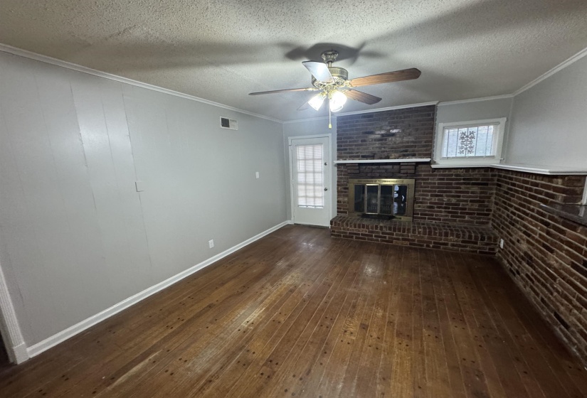 Unfurnished living room featuring brick wall, dark wood-style flooring, a brick fireplace, crown molding, and a textured ceiling