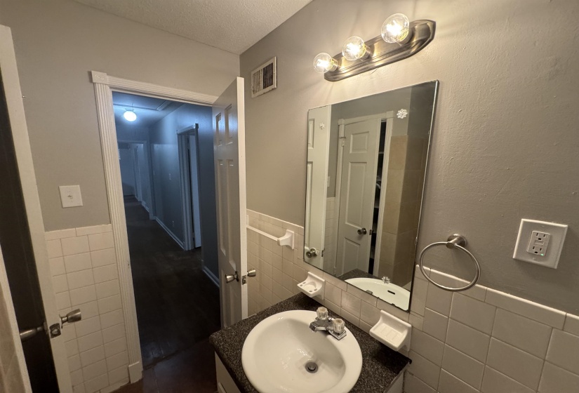 Bathroom featuring tile walls, vanity, wainscoting, and a textured ceiling