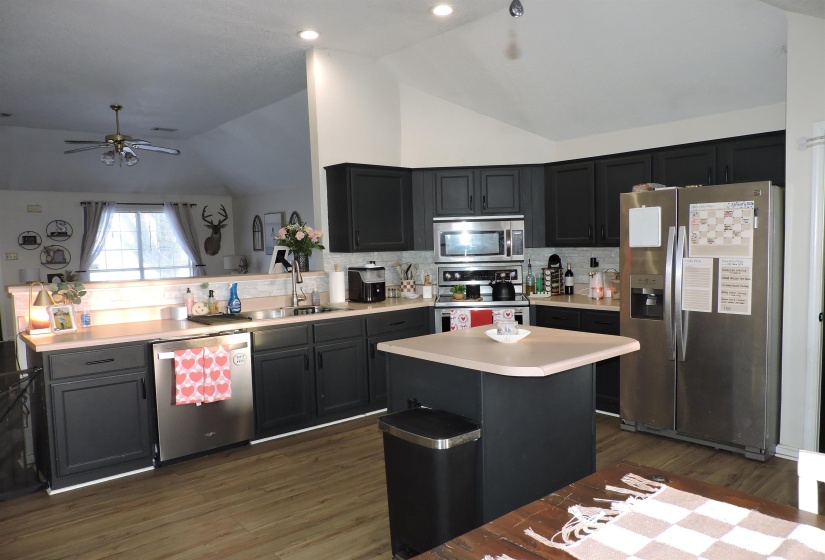 Kitchen featuring appliances with stainless steel finishes, lofted ceiling, light countertops, dark wood-style flooring, and decorative backsplash