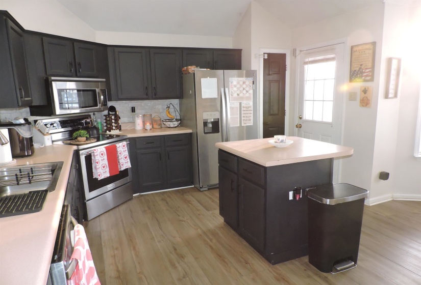 Kitchen featuring vaulted ceiling, appliances with stainless steel finishes, a kitchen island, light countertops, and light wood-style floors