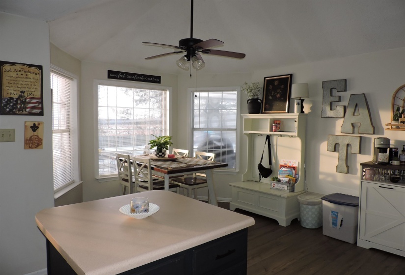 Kitchen with light countertops, dark wood-type flooring, a kitchen island, ceiling fan, and lofted ceiling