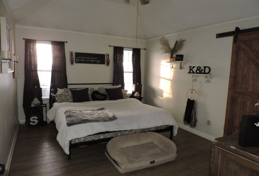 Bedroom with a barn door, dark wood-type flooring, lofted ceiling, and multiple windows