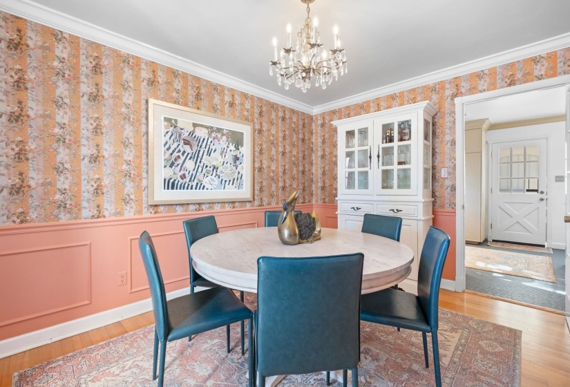 Dining space with wallpapered walls, a wainscoted wall, ornamental molding, a chandelier, and light wood-type flooring