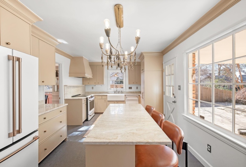 Kitchen featuring cream cabinetry, a breakfast bar, white appliances, light stone countertops, and custom range hood