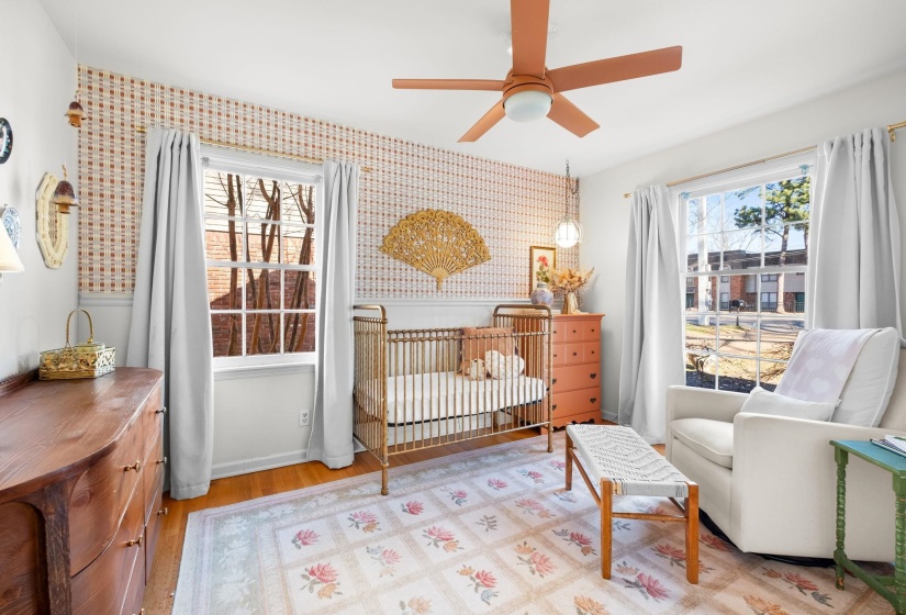 Bedroom featuring a nursery area, wood finished floors, multiple windows, and wallpapered walls