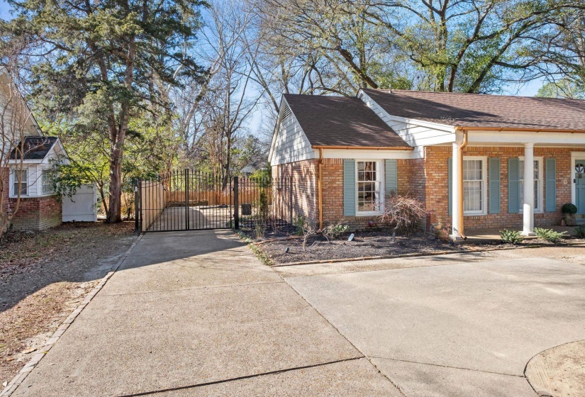 View of side of property with brick siding, a gate, concrete driveway, a shingled roof, and a porch
