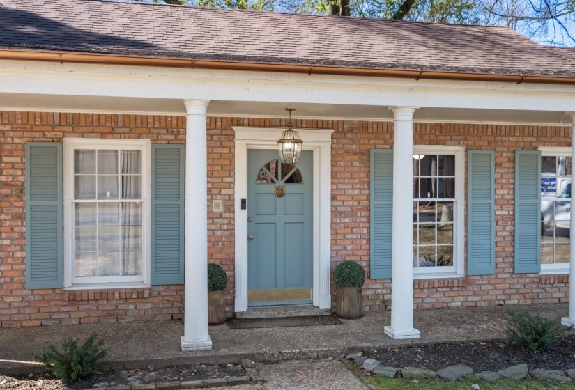 Property entrance with covered porch, roof with shingles, and brick siding