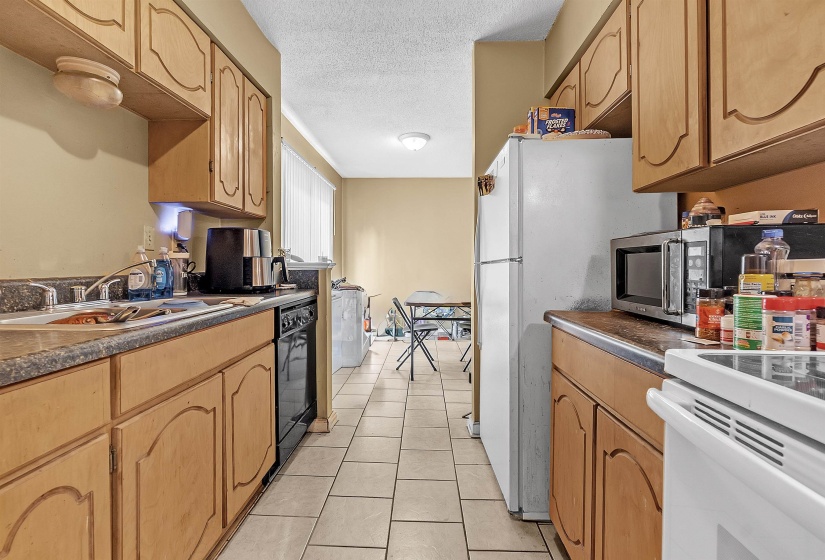 Kitchen with a textured ceiling, light tile patterned floors, dark countertops, dishwasher, and white range