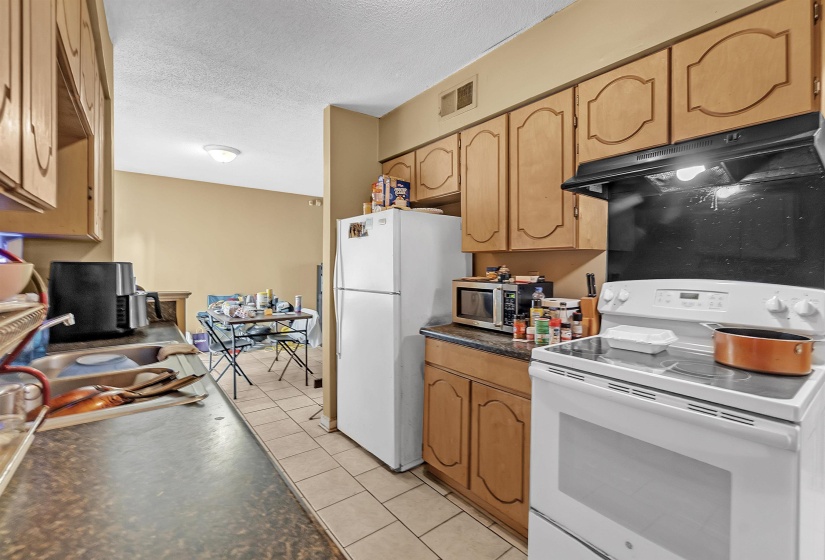 Kitchen featuring white appliances, under cabinet range hood, light tile patterned flooring, and a textured ceiling