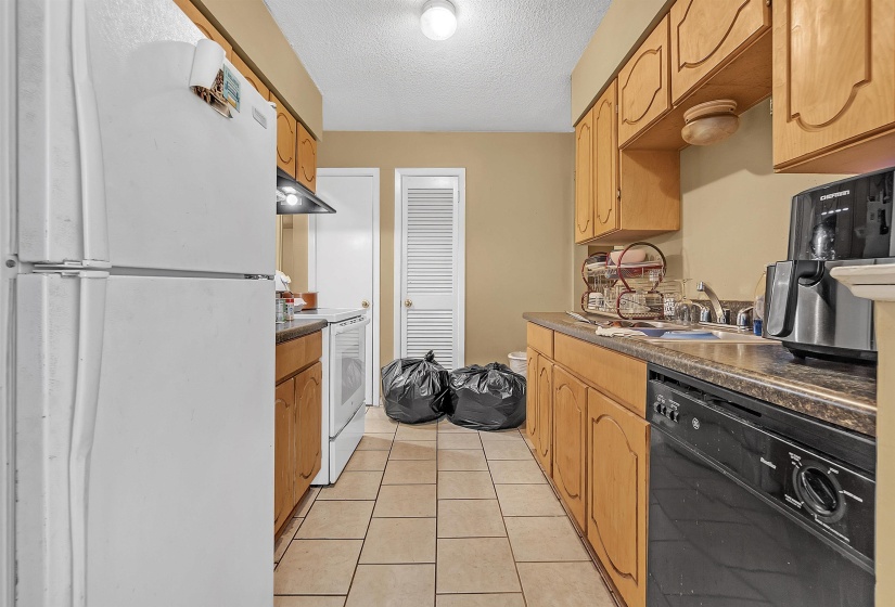 Kitchen with white appliances, a textured ceiling, light tile patterned floors, dark countertops, and under cabinet range hood