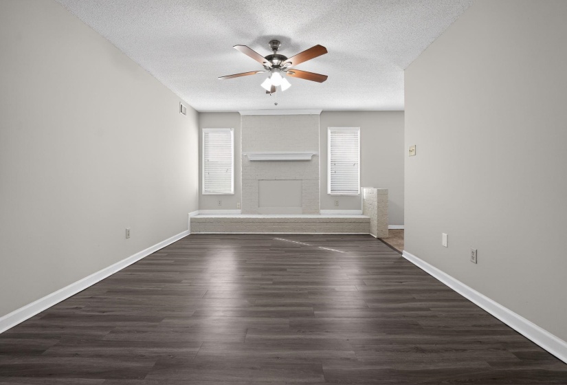 Unfurnished living room with dark wood finished floors, a brick fireplace, a textured ceiling, and a ceiling fan
