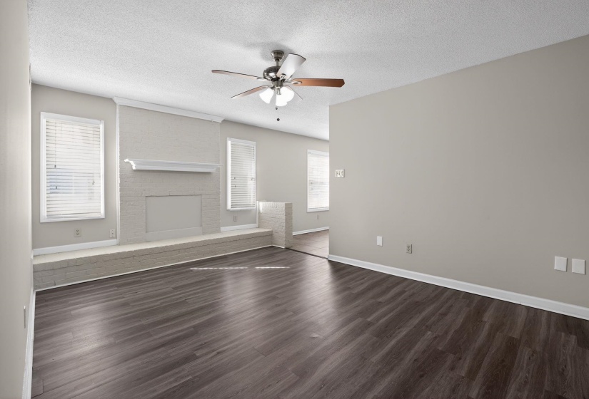 Unfurnished living room with a textured ceiling, a brick fireplace, dark wood-style flooring, and ceiling fan