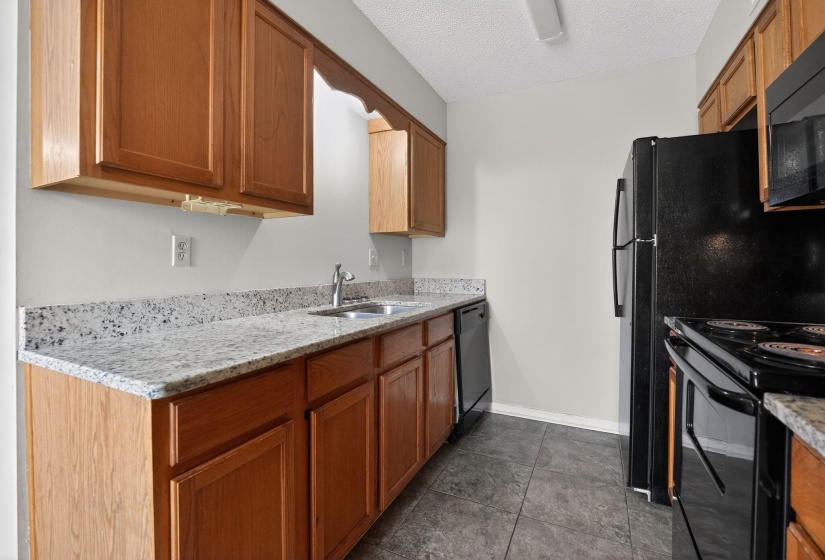 Kitchen featuring black appliances, light stone counters, a textured ceiling, brown cabinetry, and dark tile patterned floors