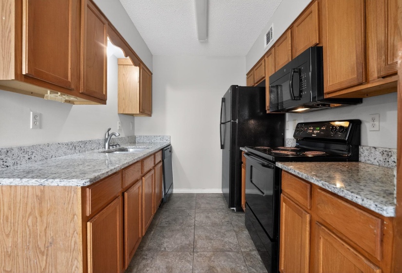 Kitchen featuring black appliances, brown cabinetry, light stone counters, and a textured ceiling