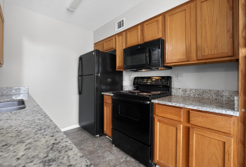 Kitchen featuring black appliances, light stone counters, brown cabinets, and a textured ceiling