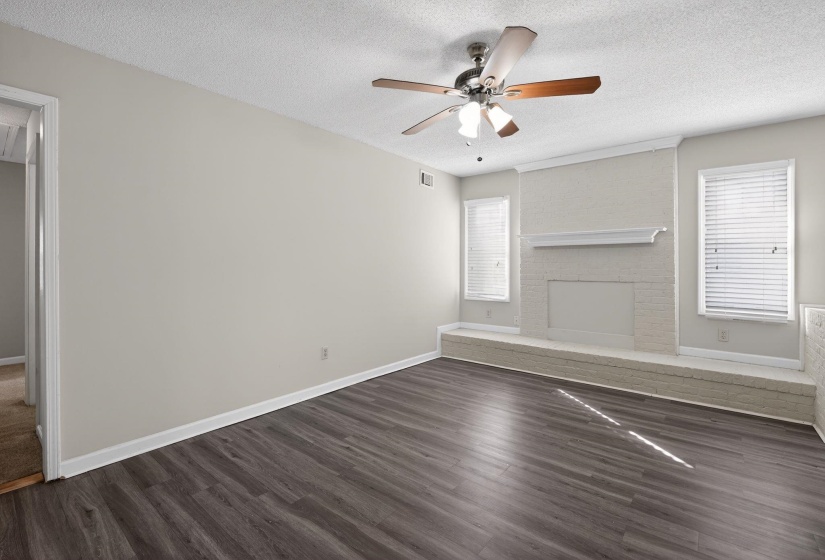 Unfurnished bedroom with a textured ceiling, dark wood finished floors, a ceiling fan, and a brick fireplace