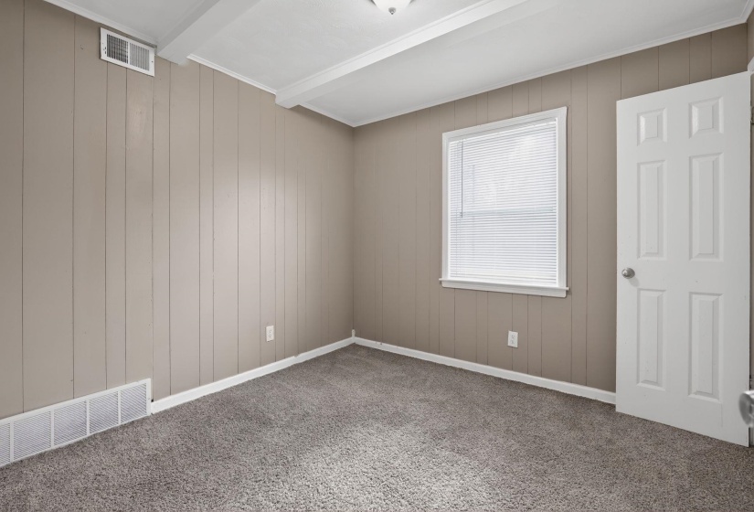 Carpeted empty room featuring wood walls and beam ceiling