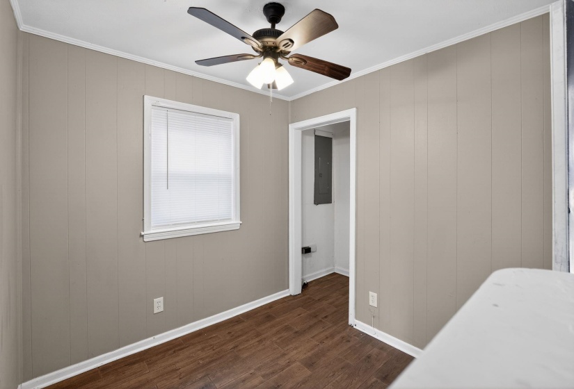 Interior space with dark wood-type flooring, wood walls, crown molding, electric panel, and ceiling fan