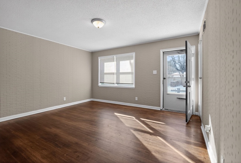 Empty room featuring dark wood-type flooring, wallpapered walls, a textured ceiling, and crown molding