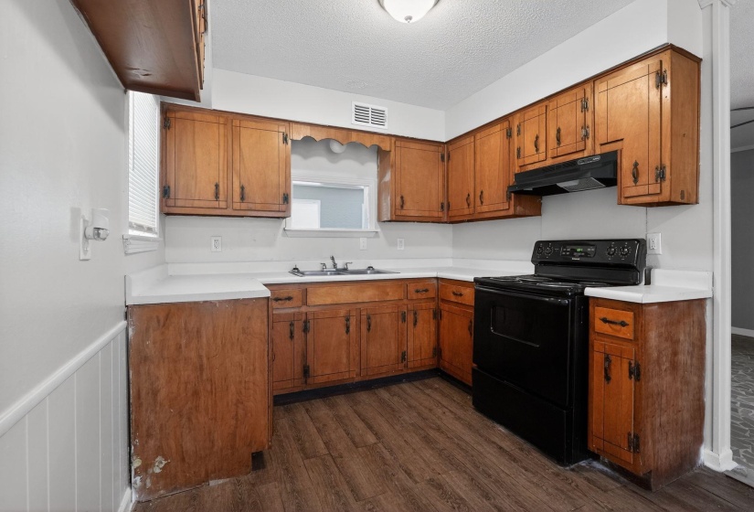 Kitchen featuring black / electric stove, brown cabinets, light countertops, a textured ceiling, and dark wood-style floors