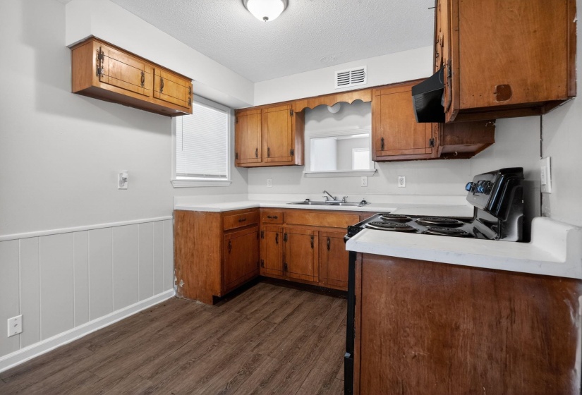 Kitchen with wainscoting, light countertops, dark wood-type flooring, a textured ceiling, and brown cabinets
