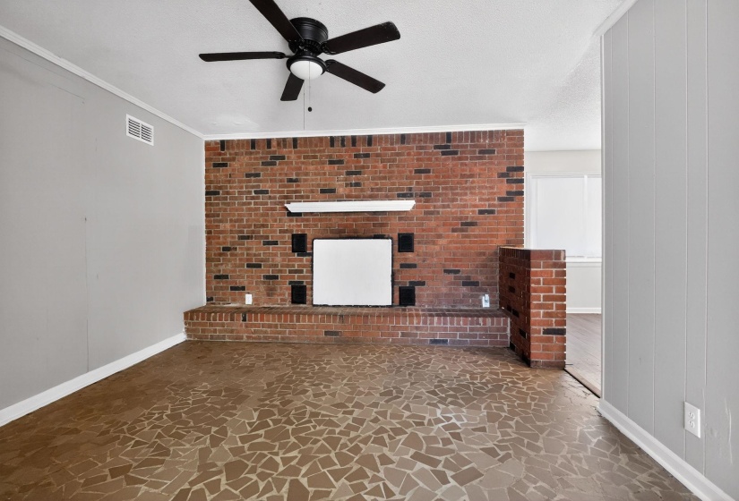 Unfurnished living room featuring stone flooring, ornamental molding, a fireplace, and a ceiling fan