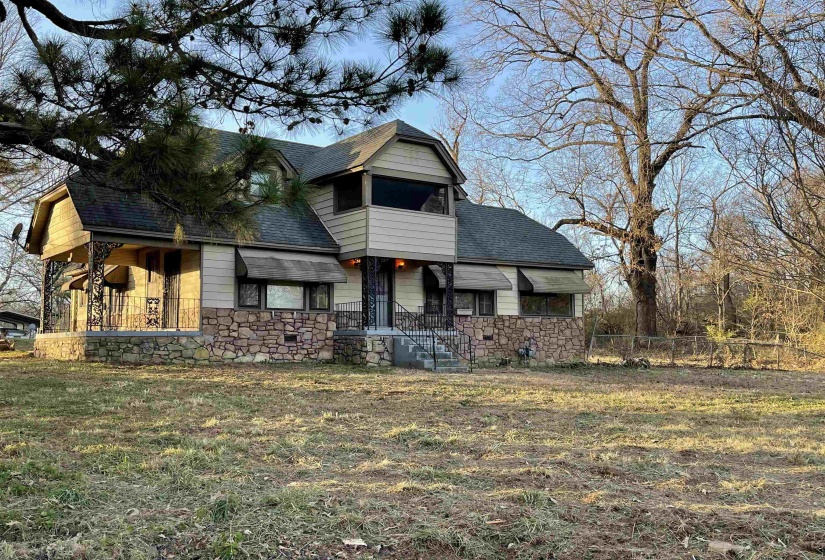 View of front of home featuring stone siding, roof with shingles and a balcony
