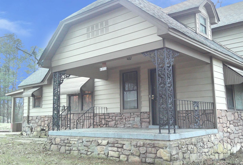 View of front facade featuring stone siding, covered porch, and a shingled roof