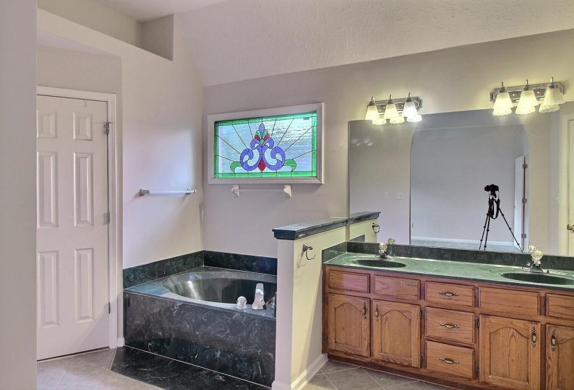 Full bath with a garden tub, double vanity, light tile patterned flooring, and lofted ceiling
