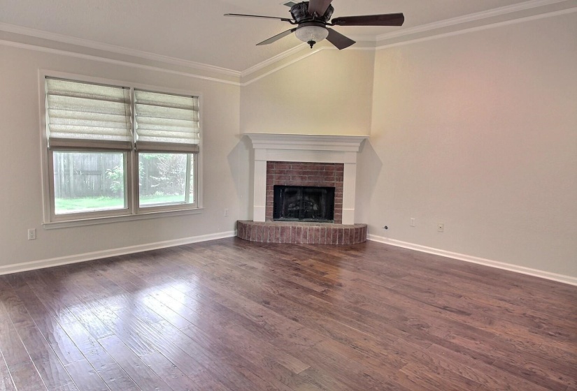 Unfurnished living room featuring crown molding, a brick fireplace, dark wood finished floors, lofted ceiling, and ceiling fan