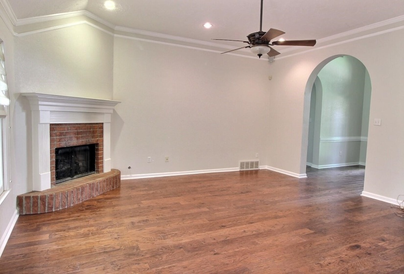 Unfurnished living room with ornamental molding, arched walkways, a brick fireplace, dark wood finished floors, and recessed lighting